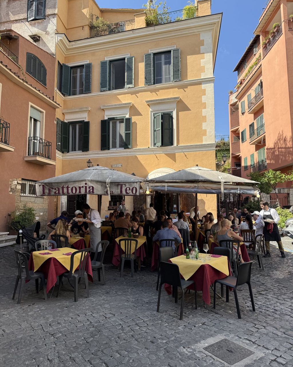 Trattoria terrace at dinner time, tables under umbrellas, diners and a Trattoria da Teo sign