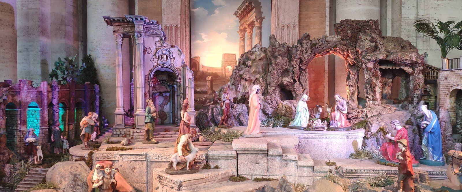 A large nativity scene: painted figures of the Holy Family, shepherds, and angels on rock scenery beneath tall stone columns.