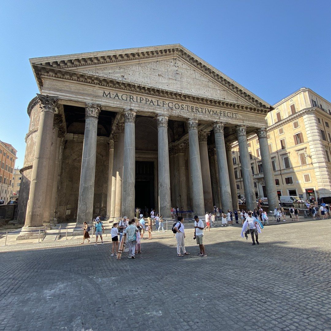 The Pantheon's full facade on a summer morning, queue barriers and visitors at the entrance for scale
