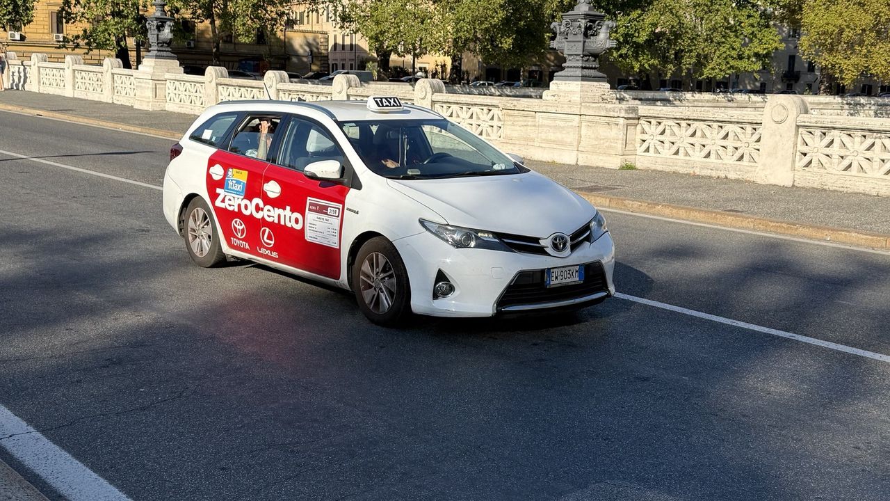 A white Rome taxi with its rooftop TAXI sign crossing a Tiber bridge