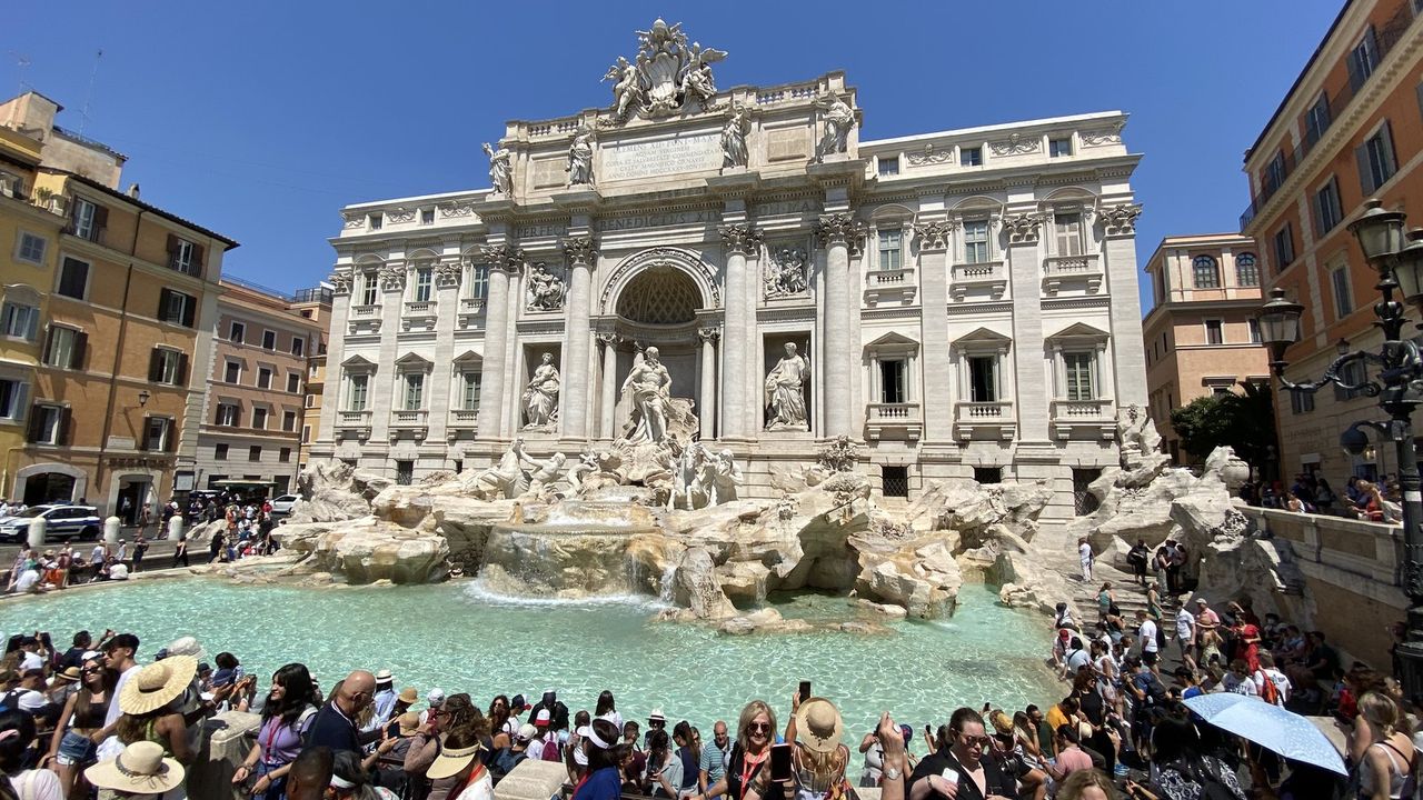The crowd packed around the Trevi Fountain basin on a summer midday