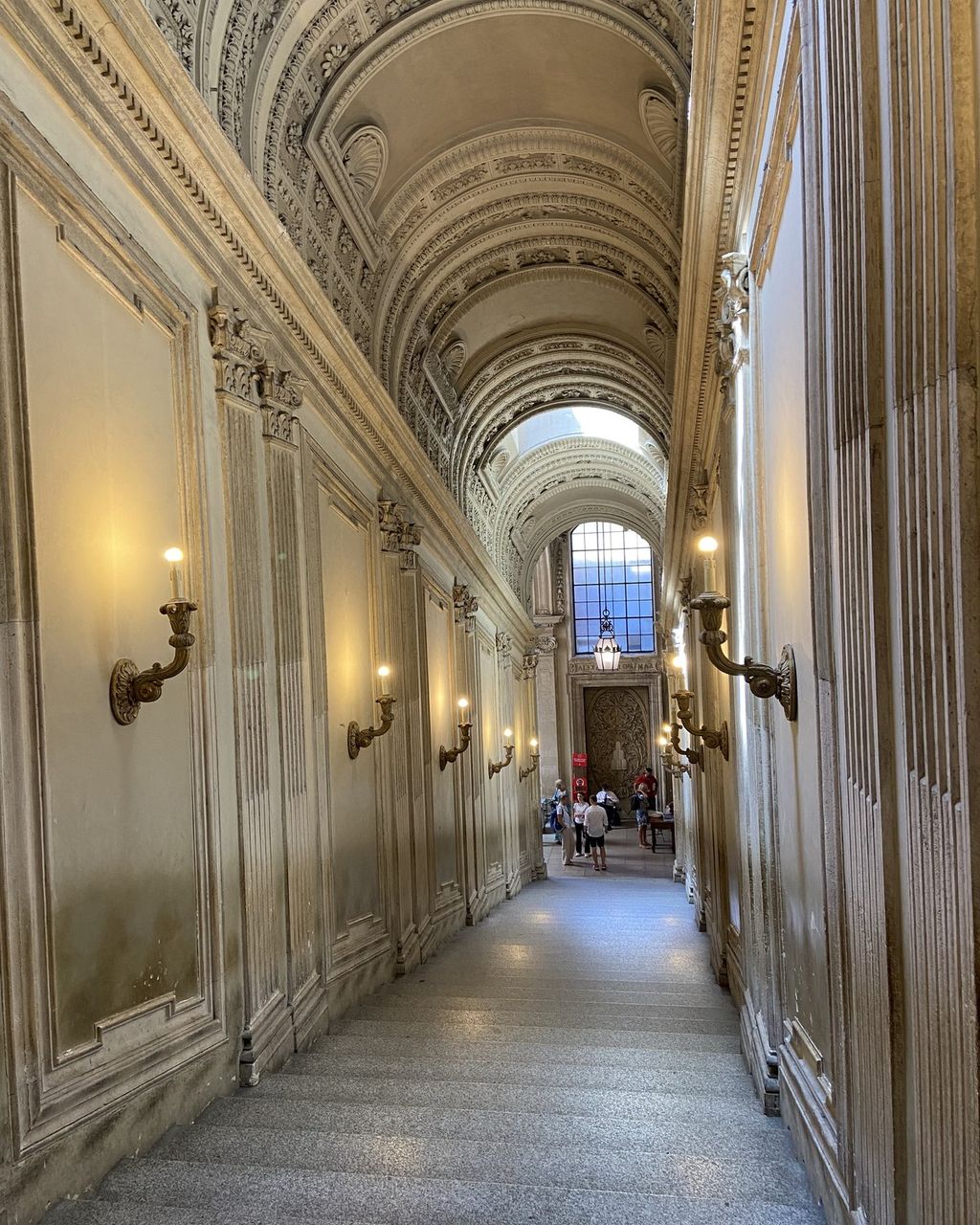 A long marble staircase corridor inside the Vatican Museums, wall lamps lit and almost nobody on the steps