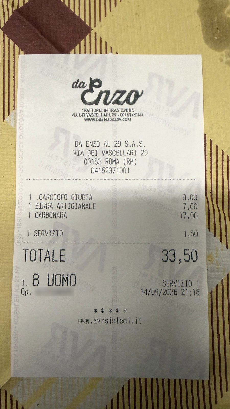A receipt on a striped tablecloth listing carciofo giudia 8.00, birra 7.00, carbonara 17.00, servizio 1.50, total 33.50.