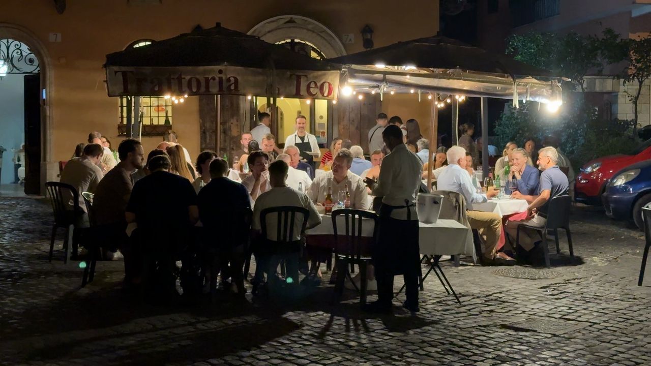 Trattoria da Teo at night, a lit sign over a canopied terrace with string lights and full tables on the cobbled piazza.