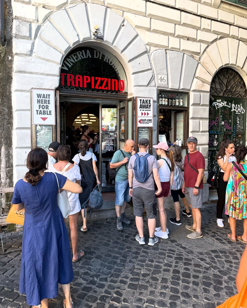 The Trapizzino shop front at Piazza Trilussa 46, an arched doorway under a Vineria di Roma sign, adults waiting outside.